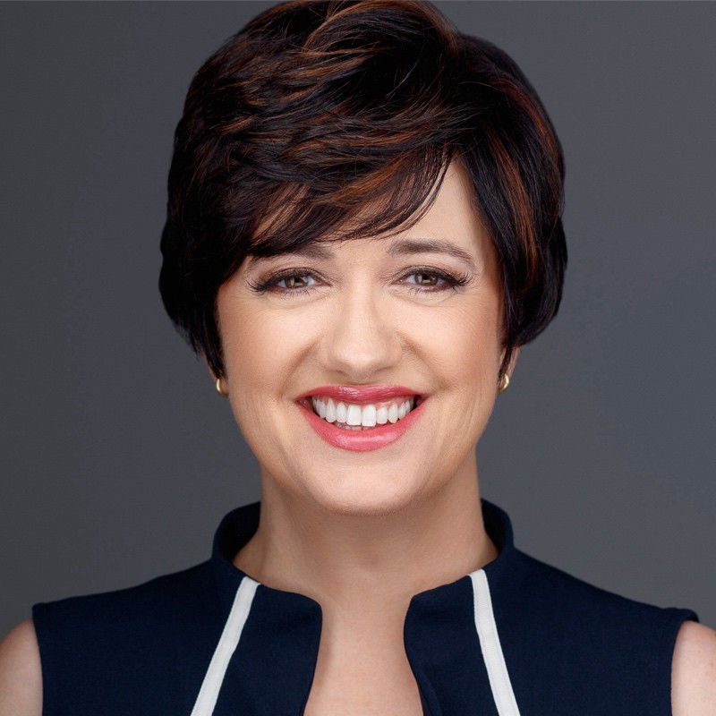 Smiling person with short dark hair, wearing a sleeveless navy top with white trim, against a gray background.