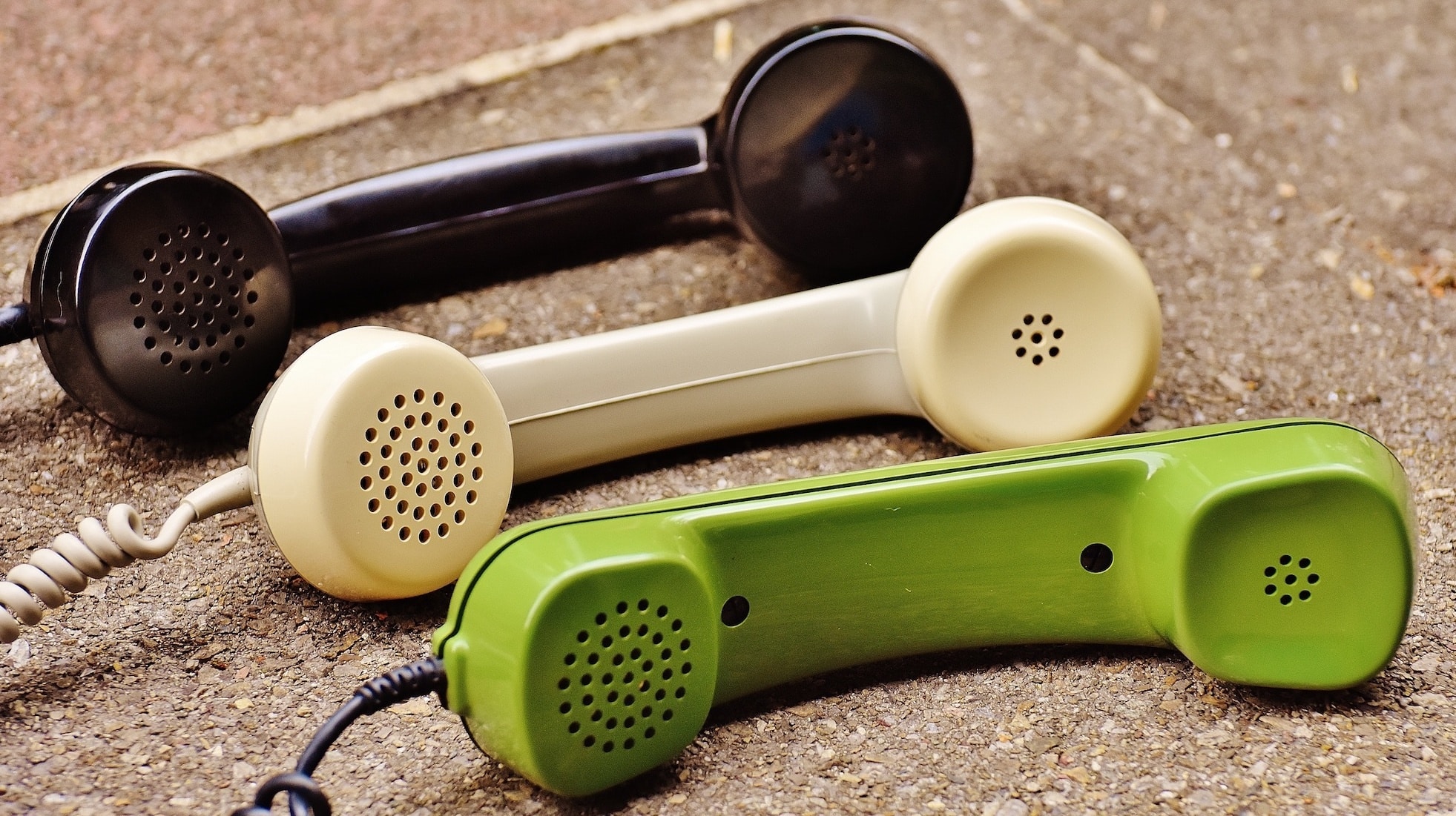Three vintage telephone handsets, one black, one beige, and one green, lie next to each other on a textured surface.