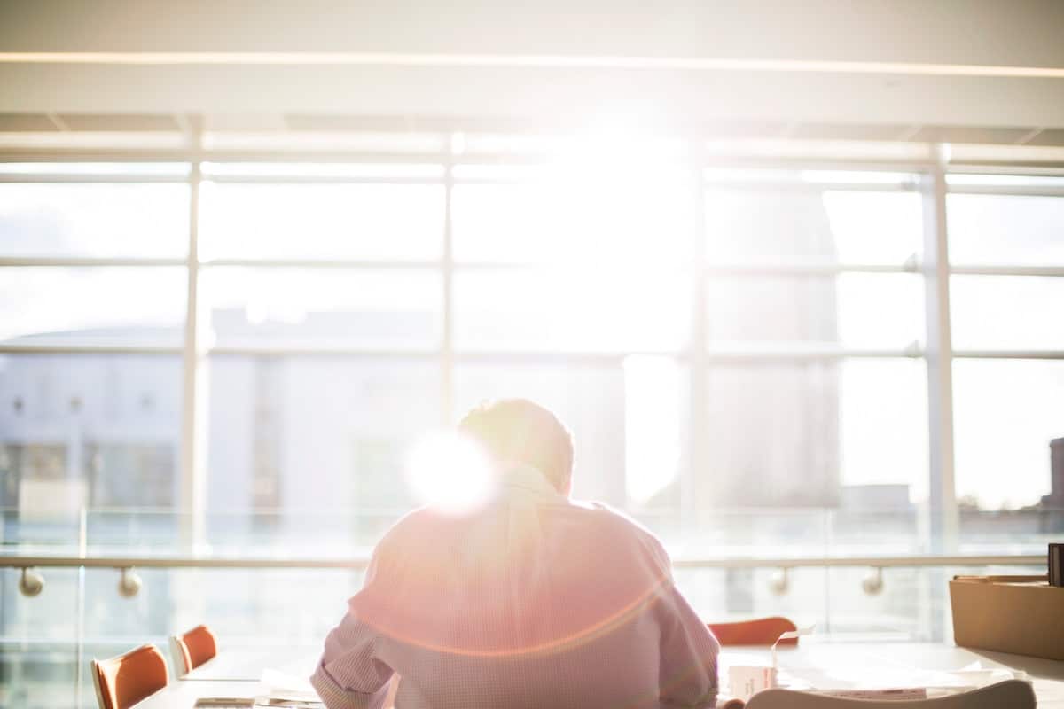 A person sitting at a desk with bright sunlight streaming through large windows in the background.