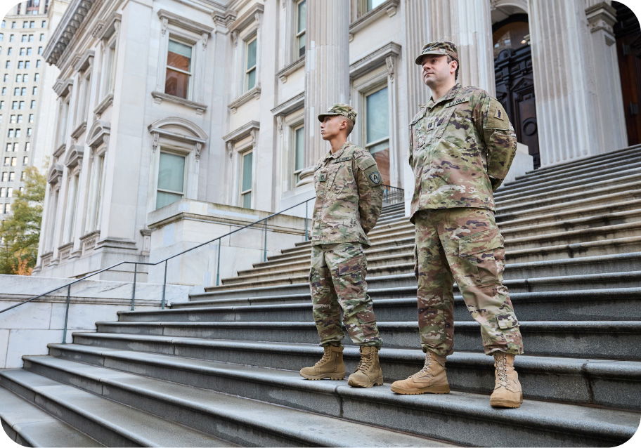Two soldiers in camouflage uniforms stand on the steps outside a government building with columns and large windows.