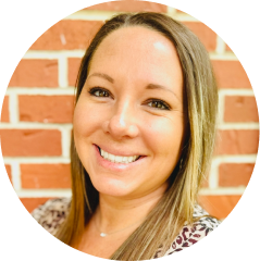 A woman with long, straight hair smiles in front of a brick wall background.